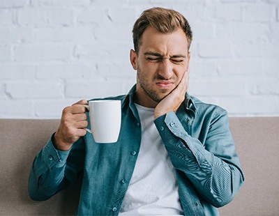 Man experiencing jaw pain while drinking coffee at home